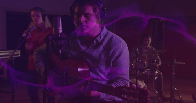 Singing lead singer wearing light shirt, playing guitar in studio with condenser mic and drums