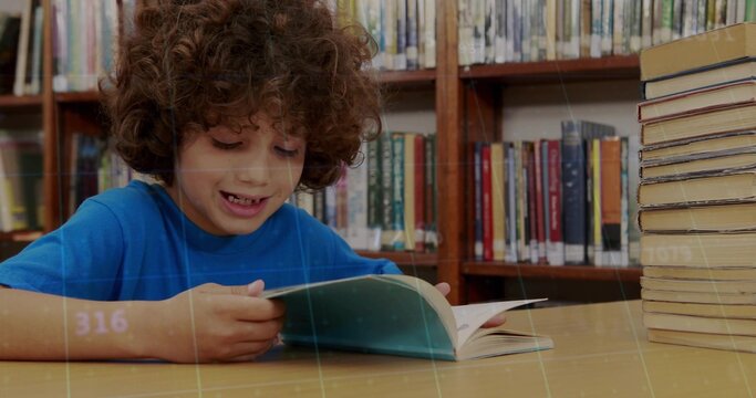 Reading boy in blue T-shirt studying open book at library table, stack of books, copy space