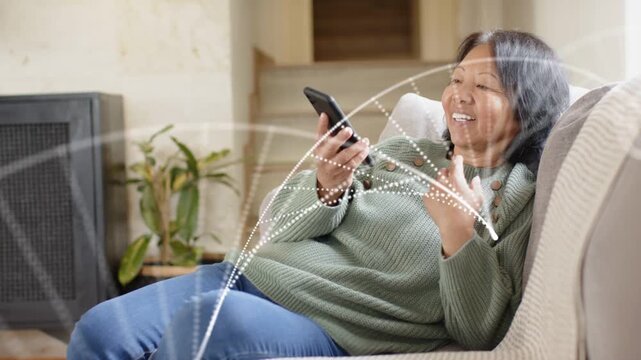 Senior woman reclining on sofa, using device and activating tech particle arcs sweeping around face