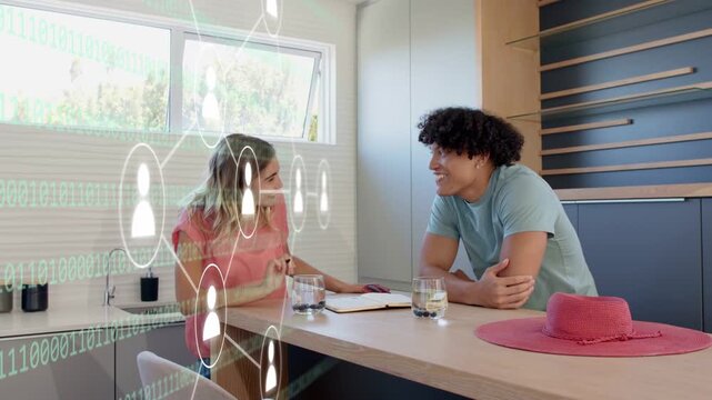 Woman gesturing pen toward notes at kitchen, man leaning, tech overlay moving, showing small object