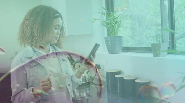 Woman holding mug and scrolling phone by window, activating overlays for tech demo, smiling at text