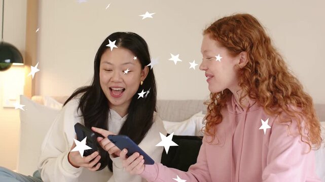 Two women on bed sharing tech right offering blue phone left tapping dark phone stars overlaying