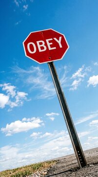 A stark red stop sign demanding obedience against a vast, cloud-dotted blue sky