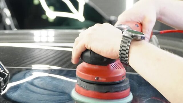 Professional Worker Buffing the Body from Light Scratches, Removing Swirls, Paint Defects from a Body of the Vehicle. A car service worker polishes the black car body with eccentric polishing machine.