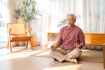 Fototapeta premium Elderly health insurance, senior man meditating in bright living room near chair and plant, calm home wellness and relaxation