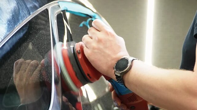 Professional Worker Buffing the Body from Light Scratches, Removing Swirls, Paint Defects from a Body of the Vehicle. A car service worker polishes the black car body with eccentric polishing machine.