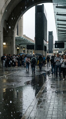Obraz premium Crowd gathered under modern city archway during rain, experiencing internet blackout and panic, reflections on wet pavement, urban street scene