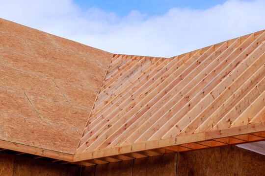 Workers build roof framework using wooden beams on new house during construction site.