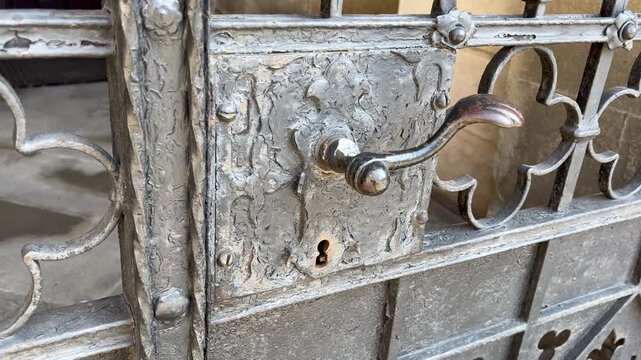 Closeup of old metal door handle on historic church gate, weathered iron surface with decorative details, vintage entrance architecture, aged texture and rustic character.