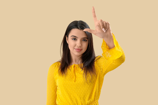 Young woman showing loser gesture on beige background