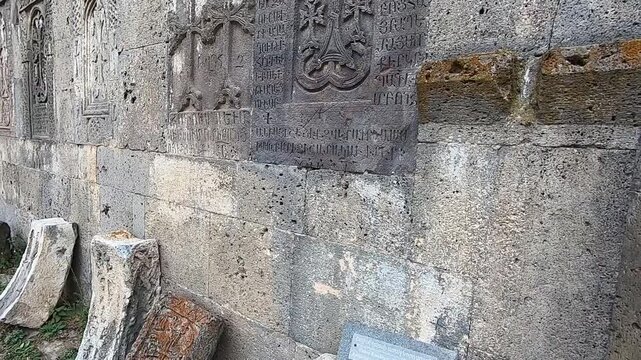  A slow pan reveals a historic stone wall adorned with intricately carved ancient Armenian khachkars. These beautiful stone crosses are a testament to rich cultural and religious heritage.
