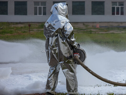 Firefighters use a foam generator to supply foam to extinguish the fire. Firefighters in protective clothing against high temperatures in a fire. Firefighters in shiny suits with foam generators.