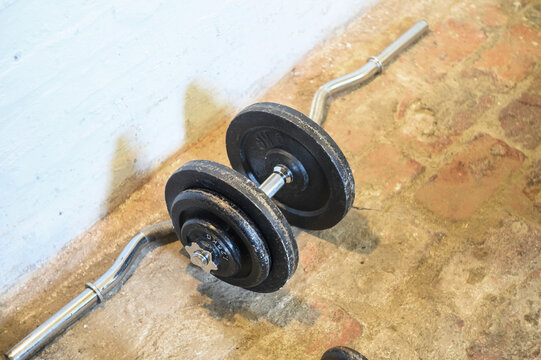 Curved barbell with weight plates resting on a textured floor near a wall
