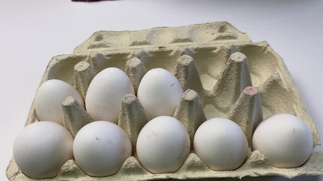 Hand arranging fresh white eggs in a carton on a kitchen surface, ready for baking or cooking.