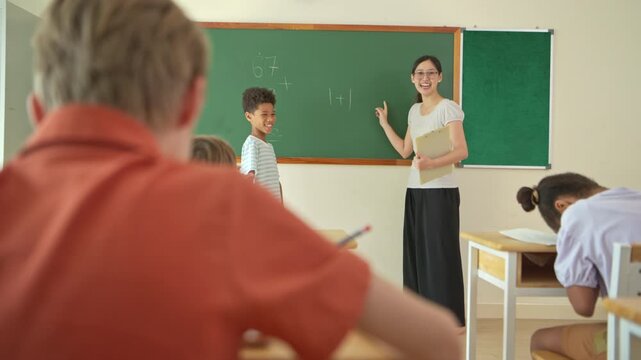 Schoolgirl solving math problem on chalkboard with teacher guidance in classroom, representing education and problem solving