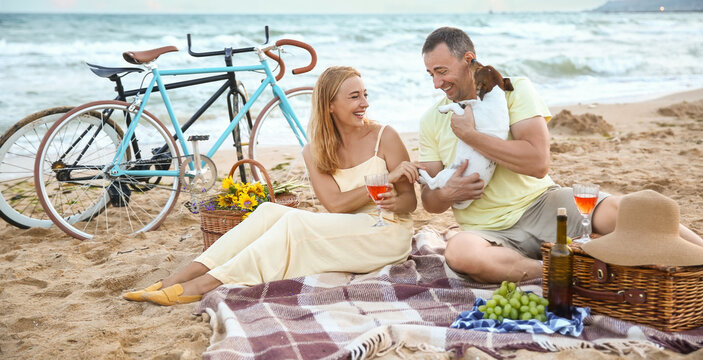 Mature couple with dog having picnic near sea on summer day