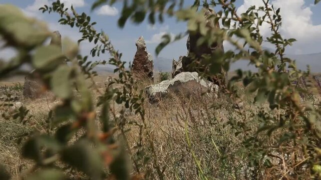 Camera pans across ancient standing stones in a mountainous landscape, revealing a close-up of a distinctive circular hole bored through a rough megalith at Zorats Karer, Armenia.
