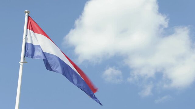 Netherlands flag waving on pole against blue sky with clouds national symbol of Holland with copy space