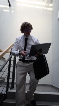 Vertical screen office worker walks on stairs using laptop and phone juggling tasks after intense workday facing burnout job loss stress failed projects and pressure adapting to digital overload and c