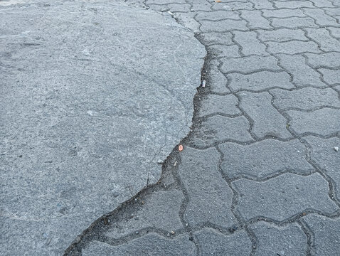 Worn pavement with cracked concrete and interlocking blocks creates a rough urban texture, showing damage, repair contrast, and aged street surface details.