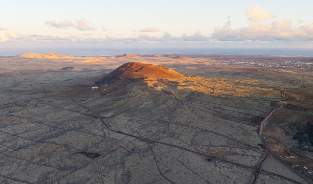 Aerial view of a majestic volcanic cone rising from the arid lava fields under a soft golden sunset sky Lanzarote, Canarias, Spain.