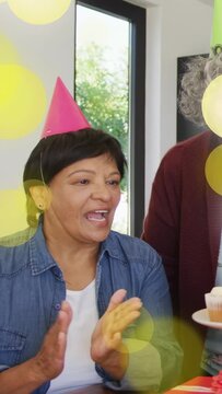 Vertical video: Woman singing while guest bringing lit cupcake, yellow bokeh floating for birthday