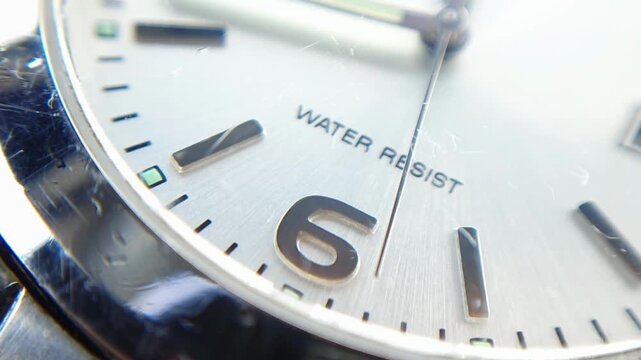 Macro view of analog watch dial with number six and water resistant text, silver metallic clock face with minute markers and hands for business schedule concepts