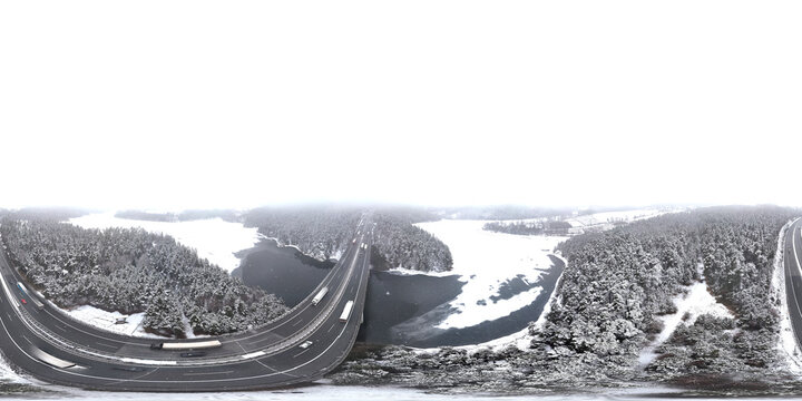 360-degree equirectangular panorama of a highway bridge crossing a dark winter river. Aerial drone view of snowy forests and infrastructure with surreal curved distortion.