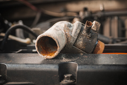 Close-up of a heavily rusted automotive pipe component on a car engine, highlighting severe corrosion, mechanical wear, and the necessity for cooling system repair and maintenance.