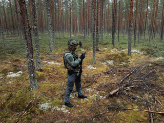 Fototapeta premium Tactical drone operator in full gear conducting forest reconnaissance using remote controller, with night vision monocular in transport position