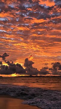 Fiery clouds ignite the horizon as the sun dips below the ocean's edge, painting the sky with vibrant hues of orange, gold, and a touch of grey.