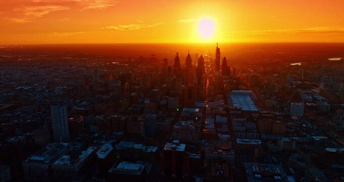 Dark cityscape of the huge metropolis partially covered with orange light of sunset. Drone footage over Philadelphia, Pennsylvania, USA at sundown.