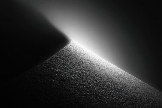Stark diagonal light illuminates textured surface meeting a dark, shadowed plane