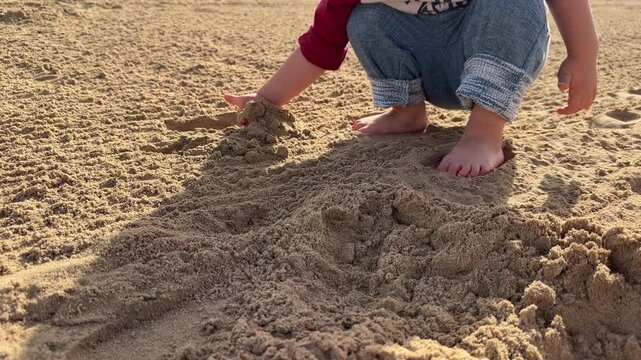 A baby digs in the sand. Little child playing on the beach. 4K.