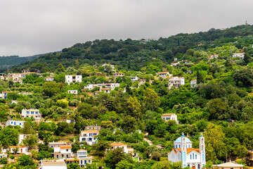 Obraz premium Karavostamo, Ikaria Greek fishing village cityscape with rolling hills mountain houses homes of Aegean island longevity blue zone at sunset