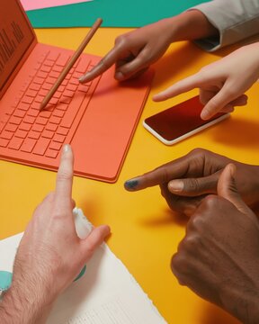 Orange laptop and diverse hands pointing at data on a colorful desk for financial audit, management consulting and creative teamwork marketing