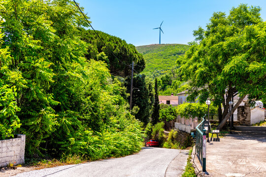 Perdiki village on Ikaria island, Greece cityscape street road of small town with house home and renewable wind energy windmill turbine