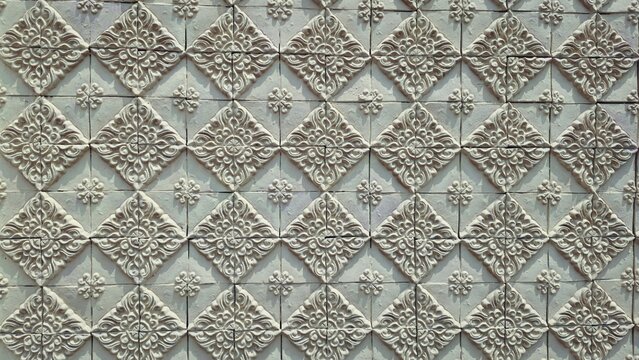 Traditional Thai floral relief pattern on yellow sandstone wall, architectural exterior texture of decorative terra cotta tiles, oriental heritage background.