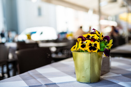Restaurant sidewalk cafe wooden table tablecloth and yellow pansies flowers pot plant in Warsaw, Poland old town in blurry blurred background
