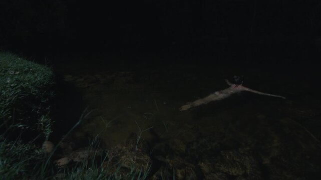 Young woman in bikini enters the river and swims at night