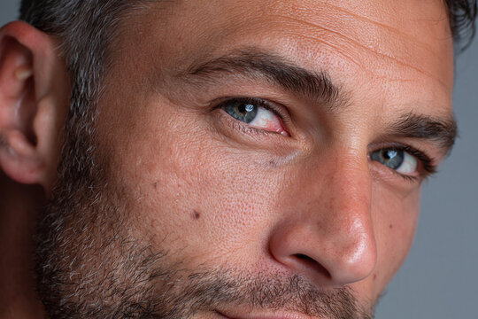 Close up of male face showing realistic skin texture pore detail blue eye stubble and facial mole conveying thoughtful expression