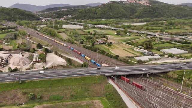 Santo Stefano di Magra, Italy - 18 April 2026: Aerial view of freight trains at Retroporto merci with colorful containers, a highway overpass, and green hills in Liguria.