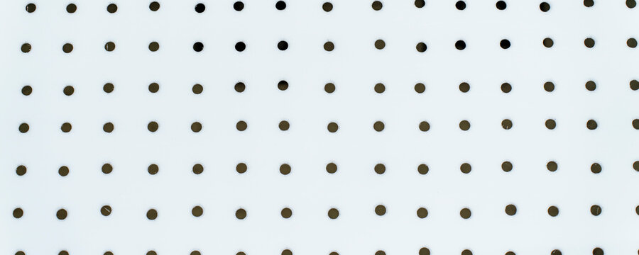 The white pegboard background features numerous dark, circular perforation holes arranged in a structured grid pattern
