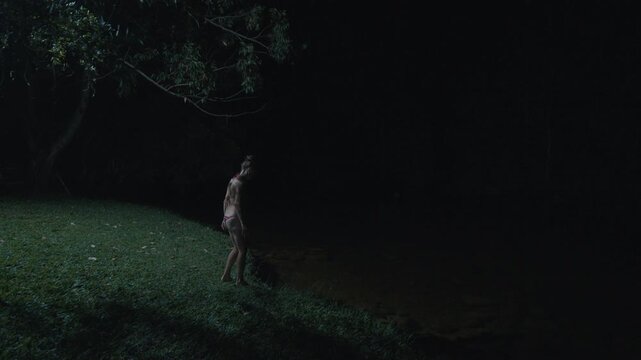Young woman in bikini enters the river and swims at night