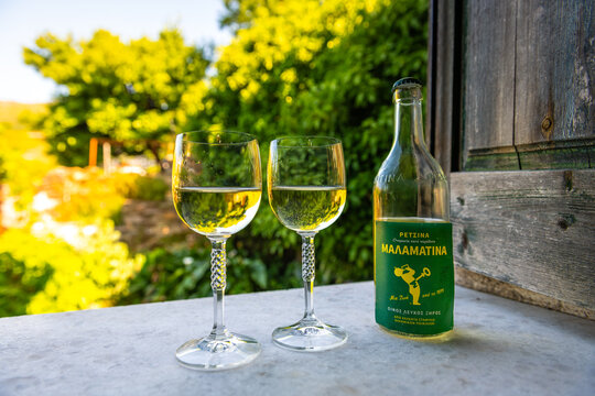Perdiki, Greece - June 21, 2023: Retsina malamatina dry Greek white wine with pine resin in glass bottle and two wineglasses on Ikaria island, Greece