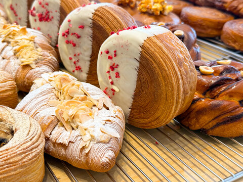 Laminated pastry rolls dipped in white chocolate with raspberry pieces arranged on bakery rack. Dessert preparation, confectionery design, sweet snack and artisan baking concept.