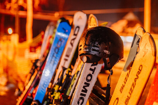 Ski equipment including Atomic skis and a black helmet lined up on a snowy slope illuminated by evening lights