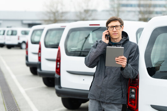 Fleet manager with digital tablet and smartphone supervising rows of white delivery vans