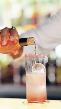 Professional bartender preparing an alcoholic beverage at the bar. Mixologist hand pouring a pink liquid from a bottle into a tall glass