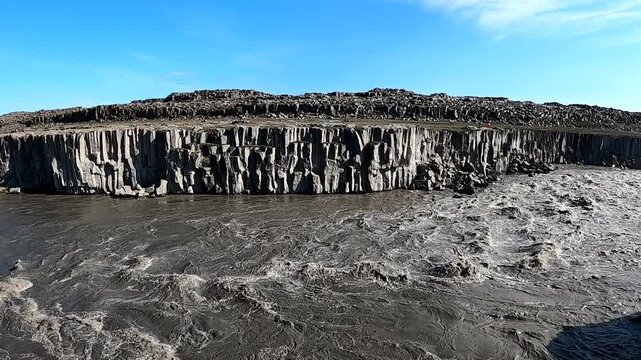 Jagged basalt cliffs and rushing glacial river at Dettifoss waterfall